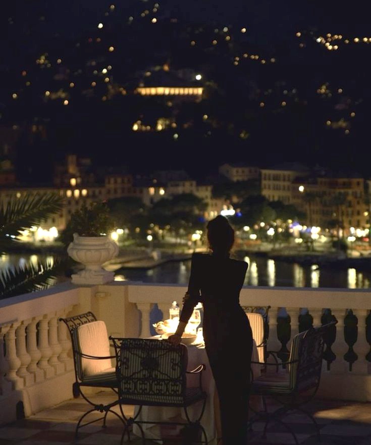 A woman on a candlelit terrace above a harbour at night